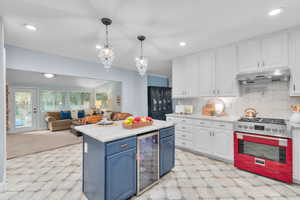 Kitchen with hanging light fixtures, blue cabinetry, white cabinets, stainless steel range oven, and beverage cooler