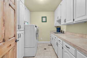 Laundry room with sink, separate washer and dryer, light tile patterned floors, and cabinets