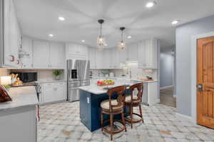 Kitchen with white cabinets, a kitchen island, hanging light fixtures, light stone counters, and high end refrigerator