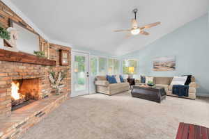 Living room with a brick fireplace, carpet, ceiling fan, and vaulted ceiling