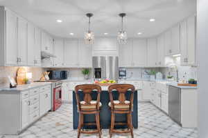 Kitchen featuring appliances with stainless steel finishes, a center island, white cabinetry, sink, and hanging light fixtures