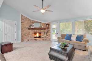 Carpeted living room featuring ceiling fan, a brick fireplace, and lofted ceiling