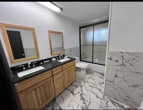 Full bathroom featuring tile walls, vanity, bath / shower combo with glass door, and toilet