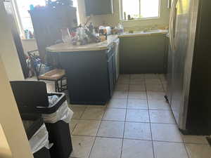 Kitchen with white dishwasher, light tile patterned floors, stainless steel fridge, and sink