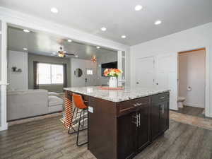 Kitchen with light stone countertops, a center island, ceiling fan, a breakfast bar, and dark brown cabinets