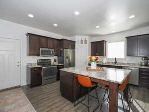 Kitchen with appliances with stainless steel finishes, light stone counters, a center island, dark hardwood / wood-style floors, and dark brown cabinetry