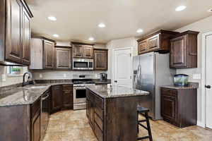 Kitchen featuring dark brown cabinets, sink, a kitchen island, a breakfast bar area, and stainless steel appliances