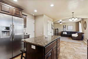 Kitchen with a kitchen island, dark stone counters, stainless steel fridge, ceiling fan, and dark brown cabinets