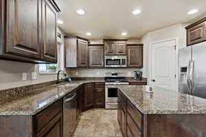 Kitchen featuring dark brown cabinets, appliances with stainless steel finishes, sink, dark stone counters, and a center island