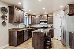 Kitchen featuring a kitchen bar, appliances with stainless steel finishes, a center island, and dark brown cabinets