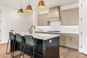 Kitchen with stainless steel gas stovetop, custom range hood, decorative backsplash, pendant lighting, and an island with sink