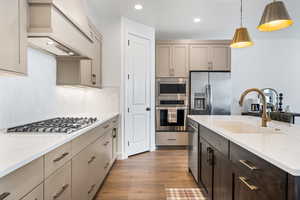 Kitchen featuring light stone countertops, appliances with stainless steel finishes, sink, hanging light fixtures, and custom range hood