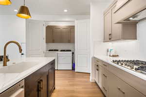 Kitchen featuring appliances with stainless steel finishes, sink, hanging light fixtures, light hardwood / wood-style flooring, and custom range hood