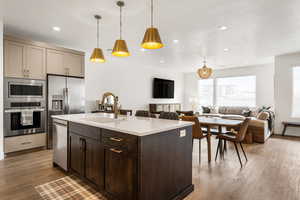 Kitchen with light stone countertops, pendant lighting, wood-type flooring, stainless steel appliances, and sink