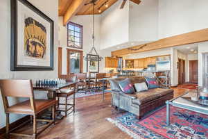 Living room with hardwood / wood-style flooring, beam ceiling, ceiling fan with notable chandelier, and a high ceiling