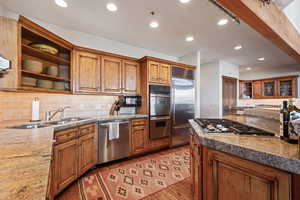 Kitchen with sink, light stone counters, light hardwood / wood-style flooring, appliances with stainless steel finishes, and backsplash