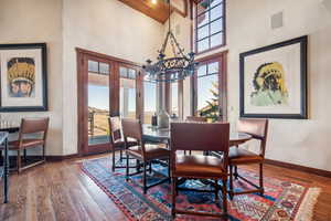 Dining space featuring french doors, wood ceiling, a notable chandelier, a towering ceiling, and hardwood / wood-style floors