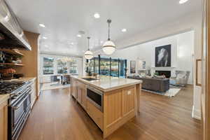 Kitchen with light brown cabinetry, extractor fan, a kitchen island with sink, sink, and double oven range