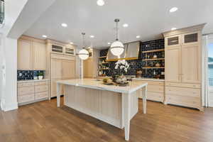 Kitchen featuring light brown cabinetry, light hardwood / wood-style floors, pendant lighting, an island with sink, and paneled refrigerator