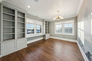 Unfurnished room featuring dark hardwood / wood-style flooring, ornamental molding, a chandelier, and a healthy amount of sunlight