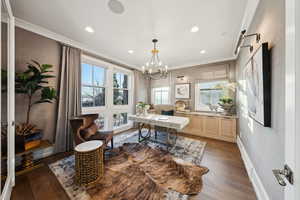 Home office with dark wood-type flooring, an inviting chandelier, and ornamental molding