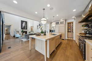 Kitchen featuring premium range hood, double oven range, a kitchen island with sink, and light brown cabinetry