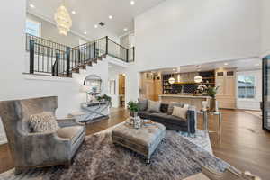 Living room with hardwood / wood-style flooring, a high ceiling, a notable chandelier, and ornamental molding