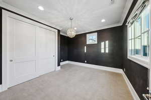 Unfurnished bedroom featuring a closet, a chandelier, crown molding, and light carpet