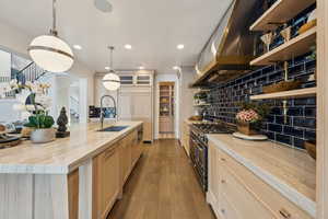 Kitchen featuring exhaust hood, decorative backsplash, decorative light fixtures, range with two ovens, and light brown cabinets