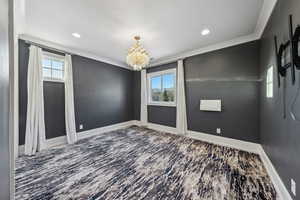 Spare room with crown molding, a healthy amount of sunlight, a textured ceiling, and a notable chandelier