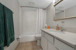 Full bathroom with a textured ceiling, tile patterned flooring, vanity, toilet, and shower / tub combo with curtain