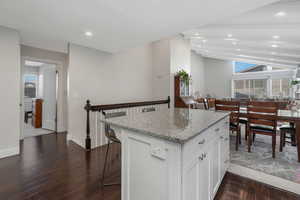 Kitchen featuring light stone counters, a breakfast bar, white cabinetry, and a healthy amount of sunlight