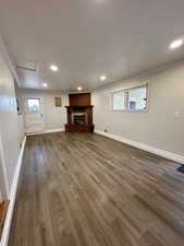 Unfurnished living room featuring hardwood / wood-style flooring, a healthy amount of sunlight, crown molding, and a brick fireplace