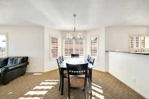 Dining area with a chandelier, a textured ceiling, and dark colored carpet