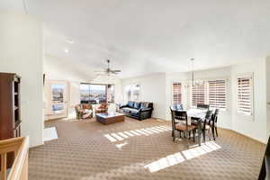 Living room with ceiling fan with notable chandelier, vaulted ceiling, light carpet, and a textured ceiling