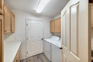 Laundry area with cabinets, a textured ceiling, washer and dryer, and light hardwood / wood-style flooring