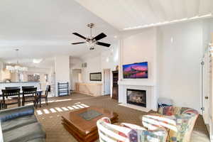 Carpeted living room featuring ceiling fan with notable chandelier and vaulted ceiling