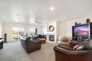 Carpeted living room featuring a tiled fireplace, ceiling fan, and a textured ceiling