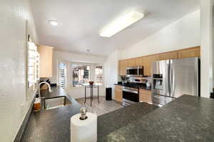 Kitchen featuring light brown cabinetry, sink, high vaulted ceiling, light wood-type flooring, and stainless steel appliances