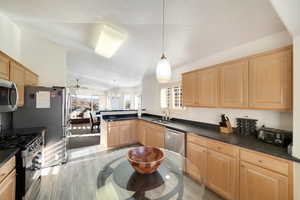 Kitchen featuring light brown cabinetry, vaulted ceiling, hanging light fixtures, kitchen peninsula, and stainless steel appliances