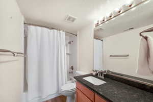 Full bathroom featuring shower / bath combo, hardwood / wood-style floors, vanity, a textured ceiling, and toilet