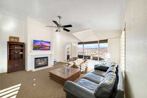 Carpeted living room with a tiled fireplace, high vaulted ceiling, and ceiling fan