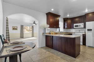 Kitchen with sink, white appliances, ceiling fan, light stone counters, and kitchen peninsula