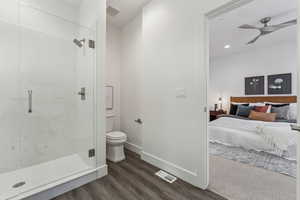 Bathroom with wood-type flooring, a shower with shower door, toilet, and ceiling fan