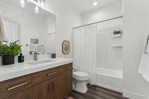 Full bathroom with shower / bathtub combination with curtain, vanity, wood-type flooring, and toilet