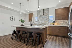 Kitchen featuring dark wood-type flooring, a breakfast bar, backsplash, a center island, and wall chimney exhaust hood