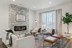 Living room with a stone fireplace and dark wood-type flooring