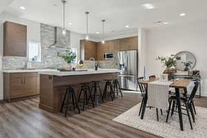 Kitchen with decorative light fixtures, dark hardwood / wood-style flooring, decorative backsplash, stainless steel appliances, and wall chimney range hood