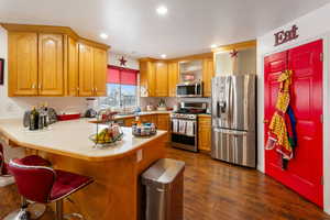 Kitchen with a kitchen bar, stainless steel appliances, sink, dark hardwood / wood-style floors, and kitchen peninsula