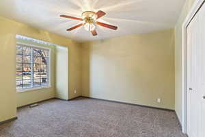 Empty room with ceiling fan, carpet, and a textured ceiling